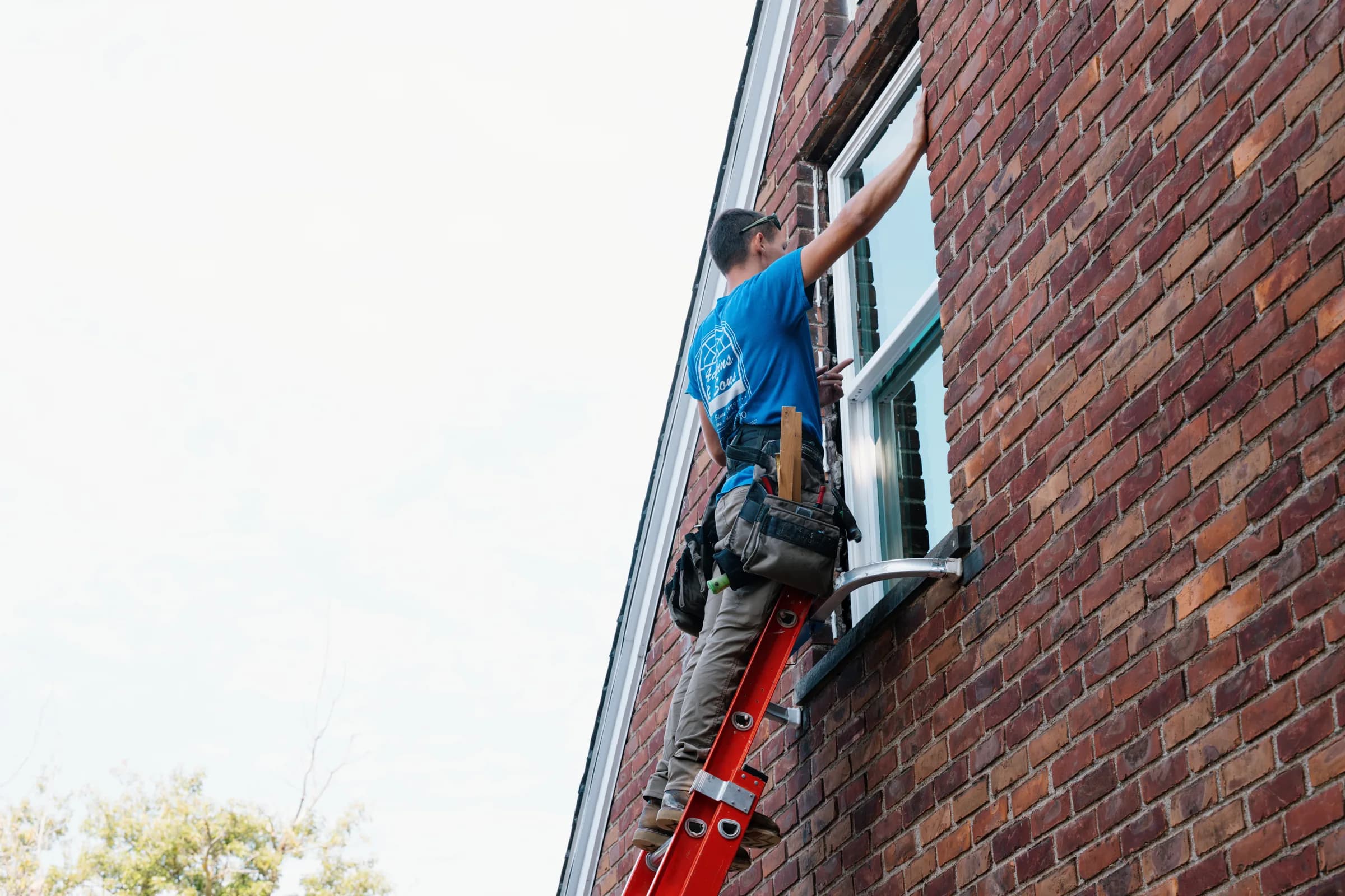 Adkins & Sons installer on a ladder setting a replacement window in a brick wall