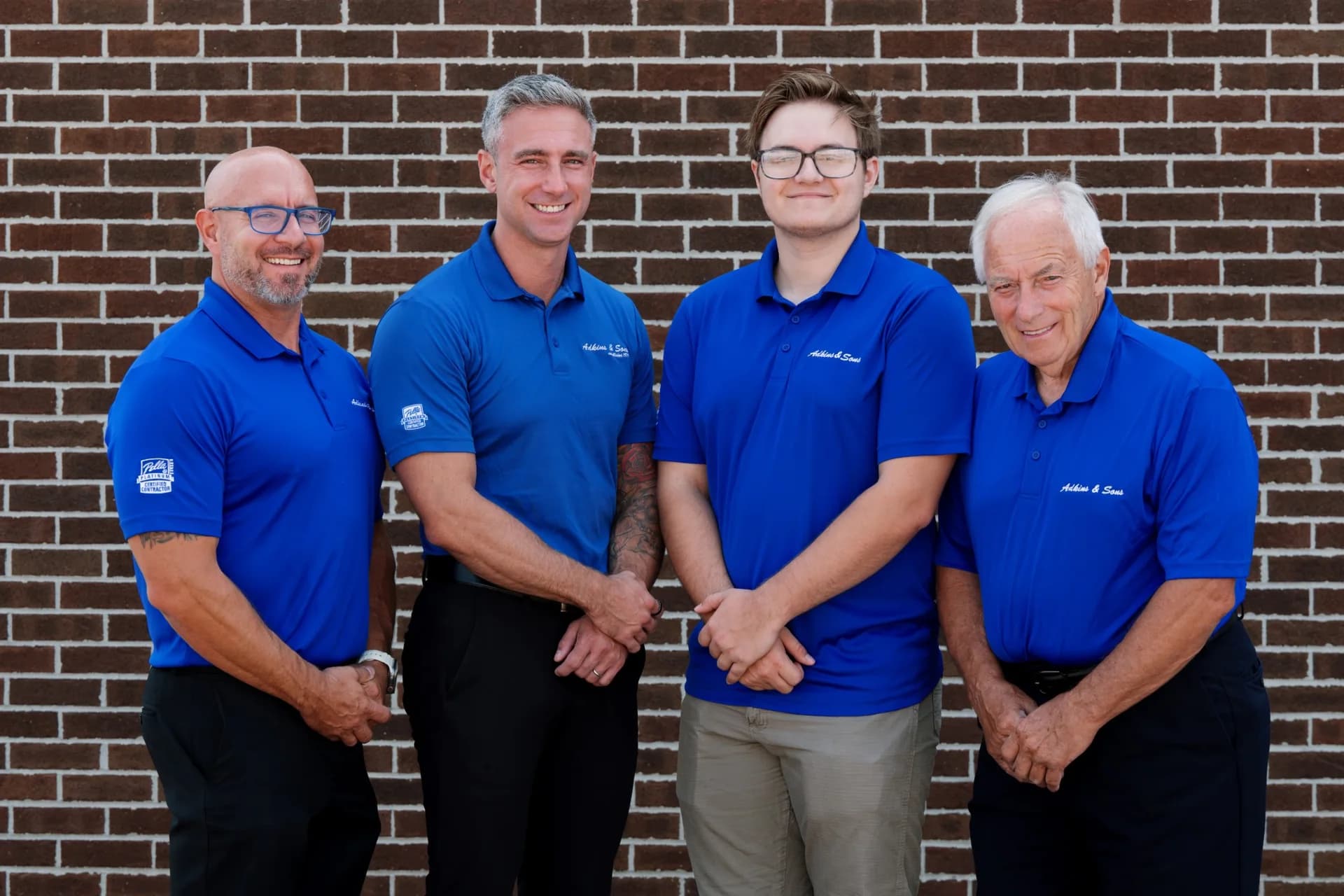Kyle Adkins Jr., Phil Adkins, Owen Adkins and Kyle Adkins Sr. in Adkins & Sons polos against a brick wall