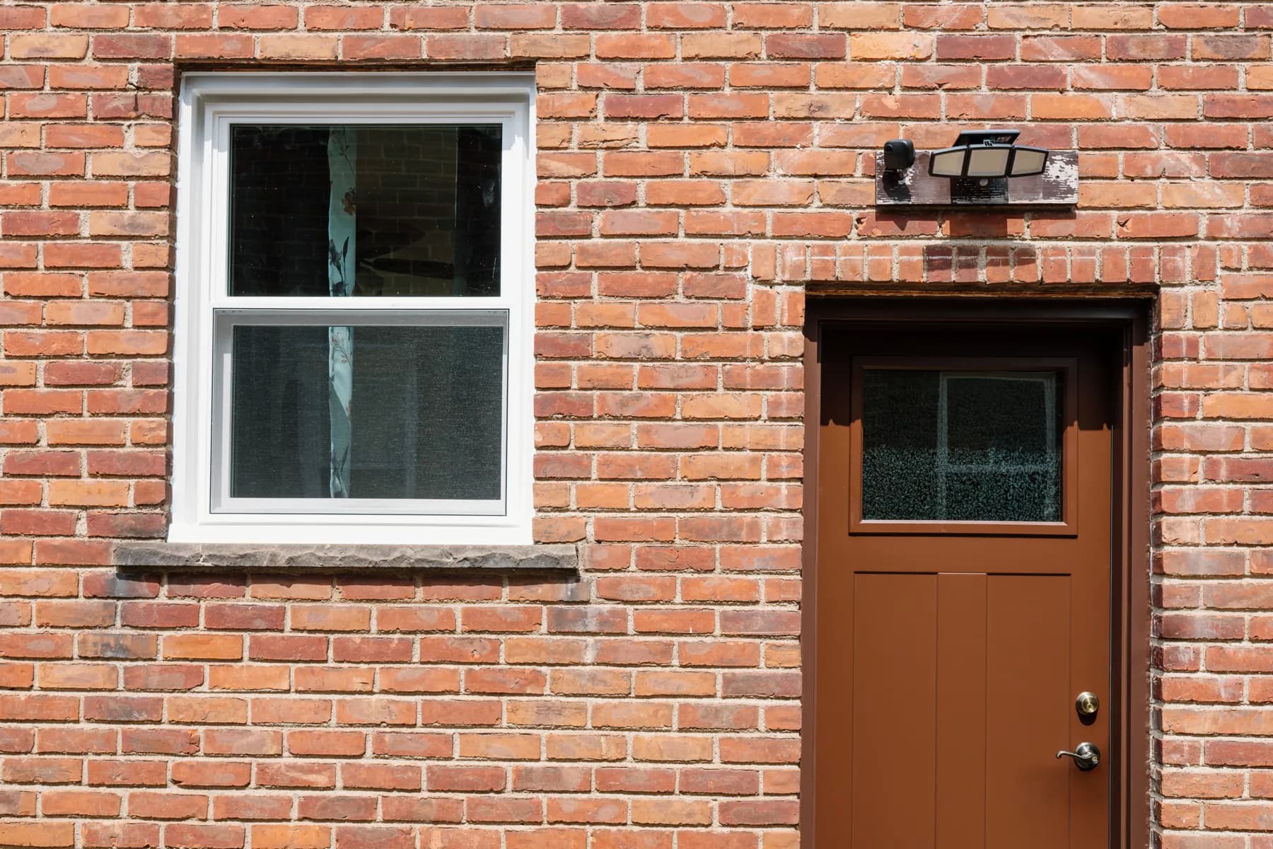 White double-hung window and a new brown entry door on a Southgate brick home