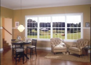Bank of four large double-hung windows in viewed from sitting room with easy chairs and a card table
