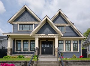 Contemporary two-story home with hint of bungalow style sporting dark gray siding, black-frame windows, black entry door with windows and sidelights