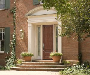 Lovely medium-brown simulated-wood front door flanked by sidelights and off-white trim at entrance of vintage brick home