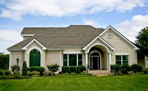 Upscale home with tan lap siding and brick facade, lots of different window styles, and a dark woodgrain door with sidelights on each side and a round-top window above