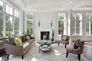 Sunny living area with sofa, chairs, and a fireplace rimmed by several sets of double-hung windows